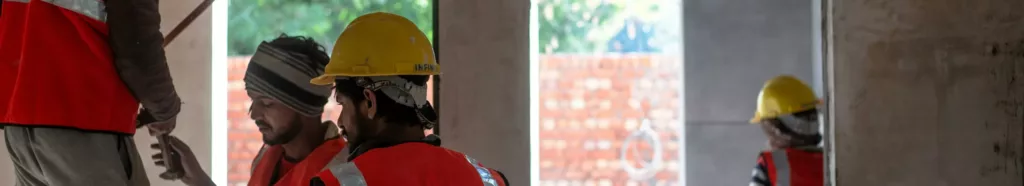 Construction workers wearing safety gear at an indoor building site in Delhi.