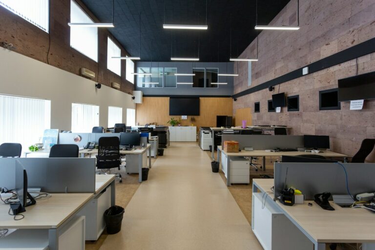Grand bureau en open space vide, avec des rangées de postes de travail et d’écrans sous un éclairage suspendu