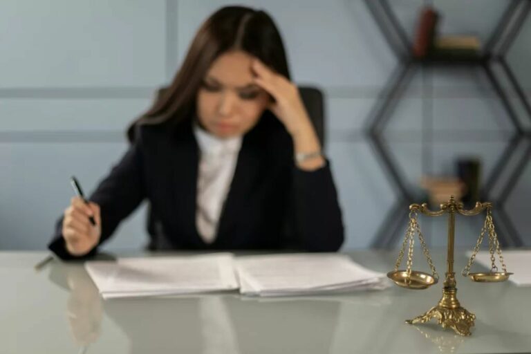 Juriste fatiguée relisant des documents près d’une balance de la justice