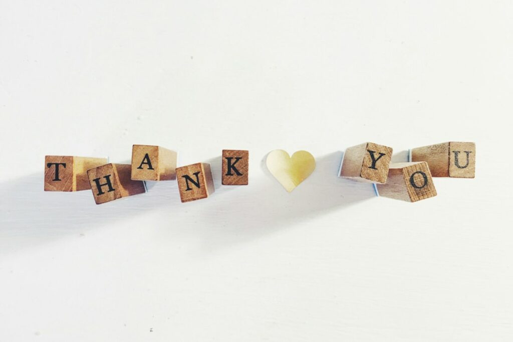 Cubes en bois formant les mots thank you autour d’un petit cœur, sur fond blanc