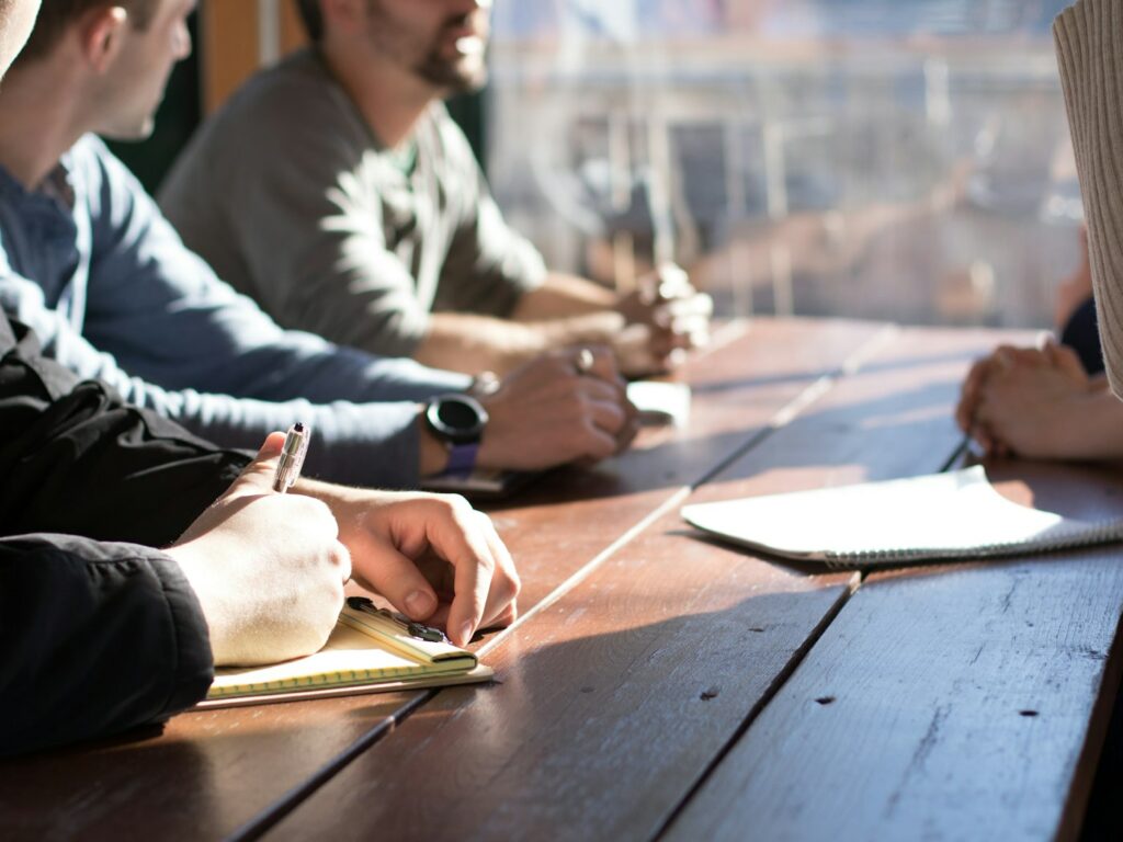 Personnes en réunion autour d’une table, carnets et stylos en main