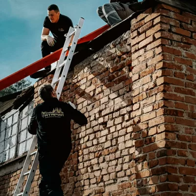 Three men repairing a brick wall outdoors on a sunny day. Teamwork and construction concept.